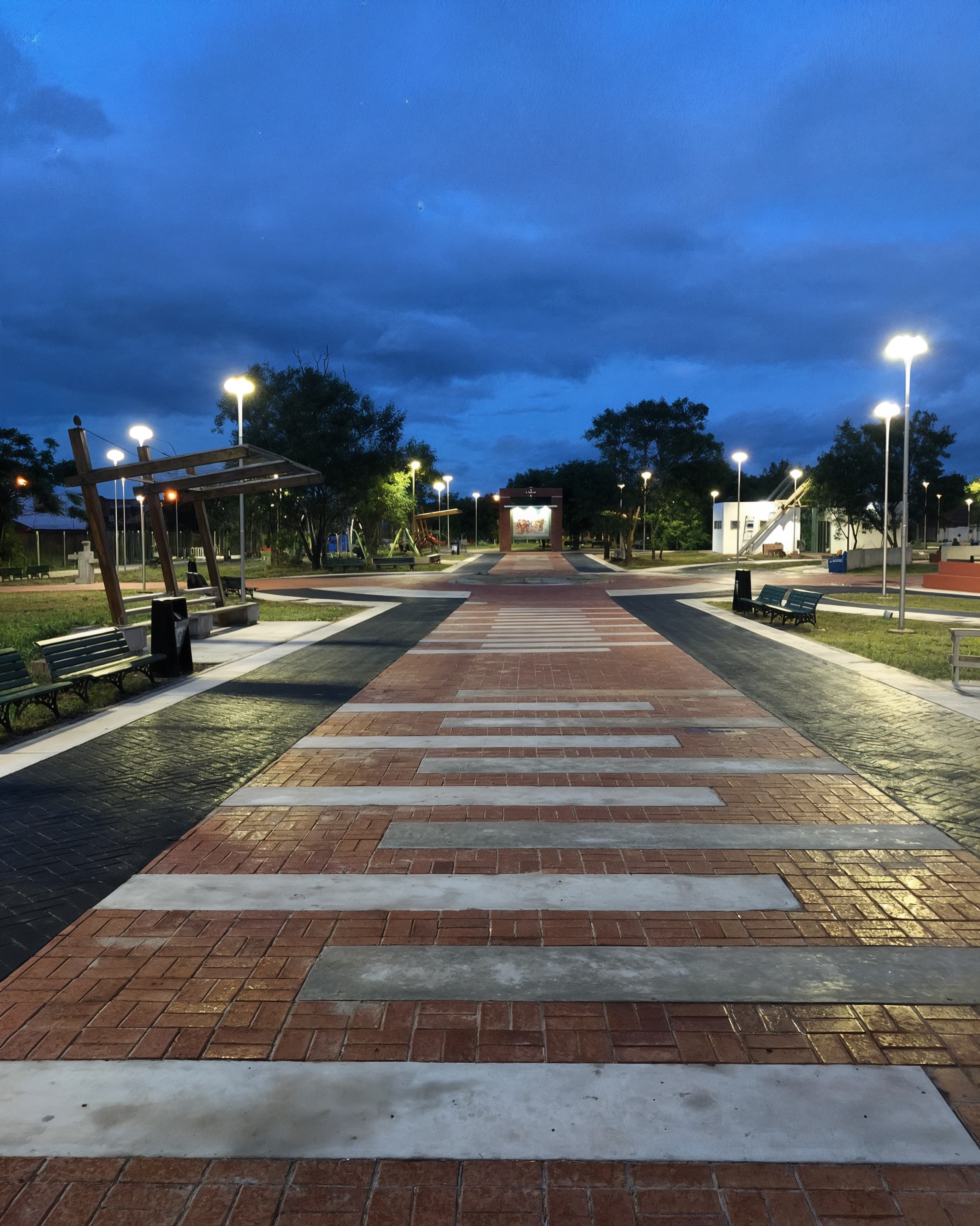 Plaza Virgen de Cotoca iluminada al anochecer, con sus caminos de ladrillo y luminarias